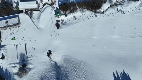 high altitude top down shot of bottom of ski run, skiers arriving at base of mountain lining up for the chairlifts