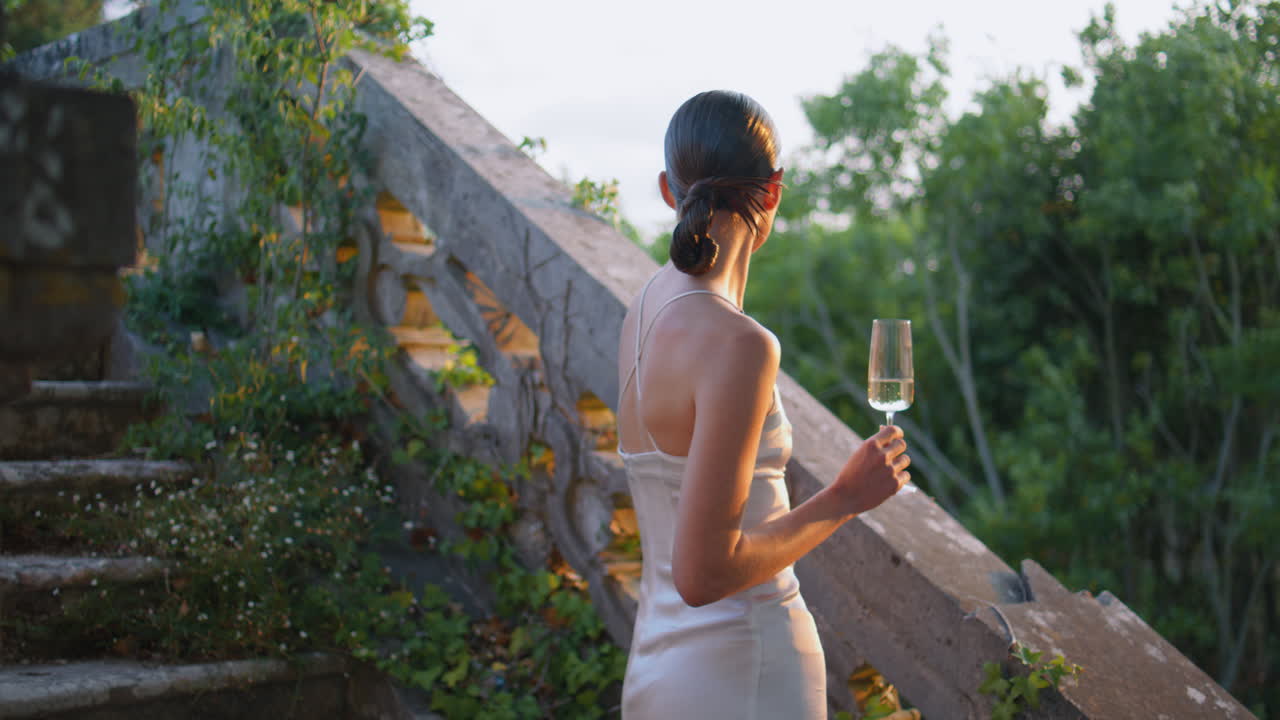 mujer soñadora relajando un vaso de vino en las escaleras del antiguo palacio. mujer disfrutando de la luz del sol
