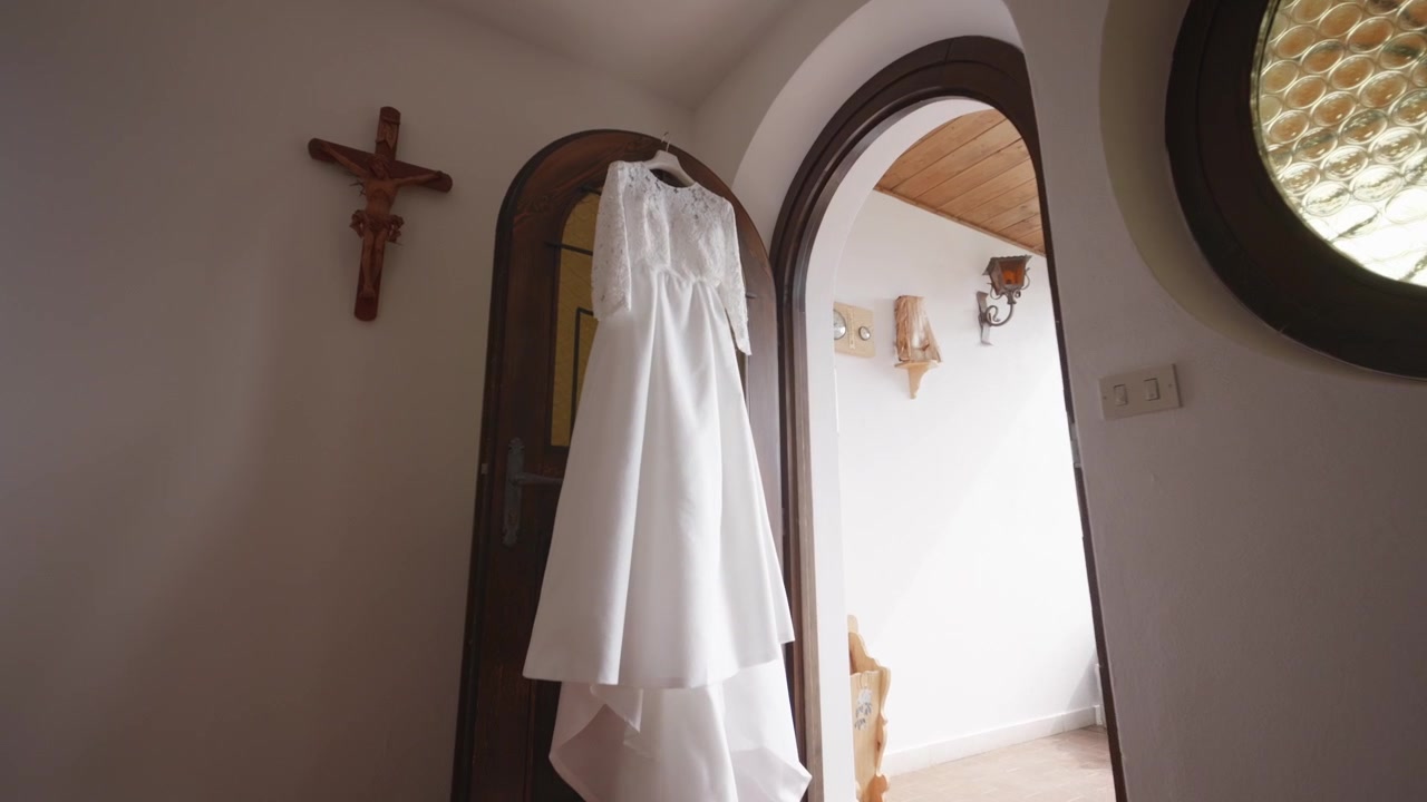 Vestido de novia colgando en el interior antes de la ceremonia. Elegante traje nupcial preparado para el día especial, iluminado por luz natural en un entorno de hogar tradicional.