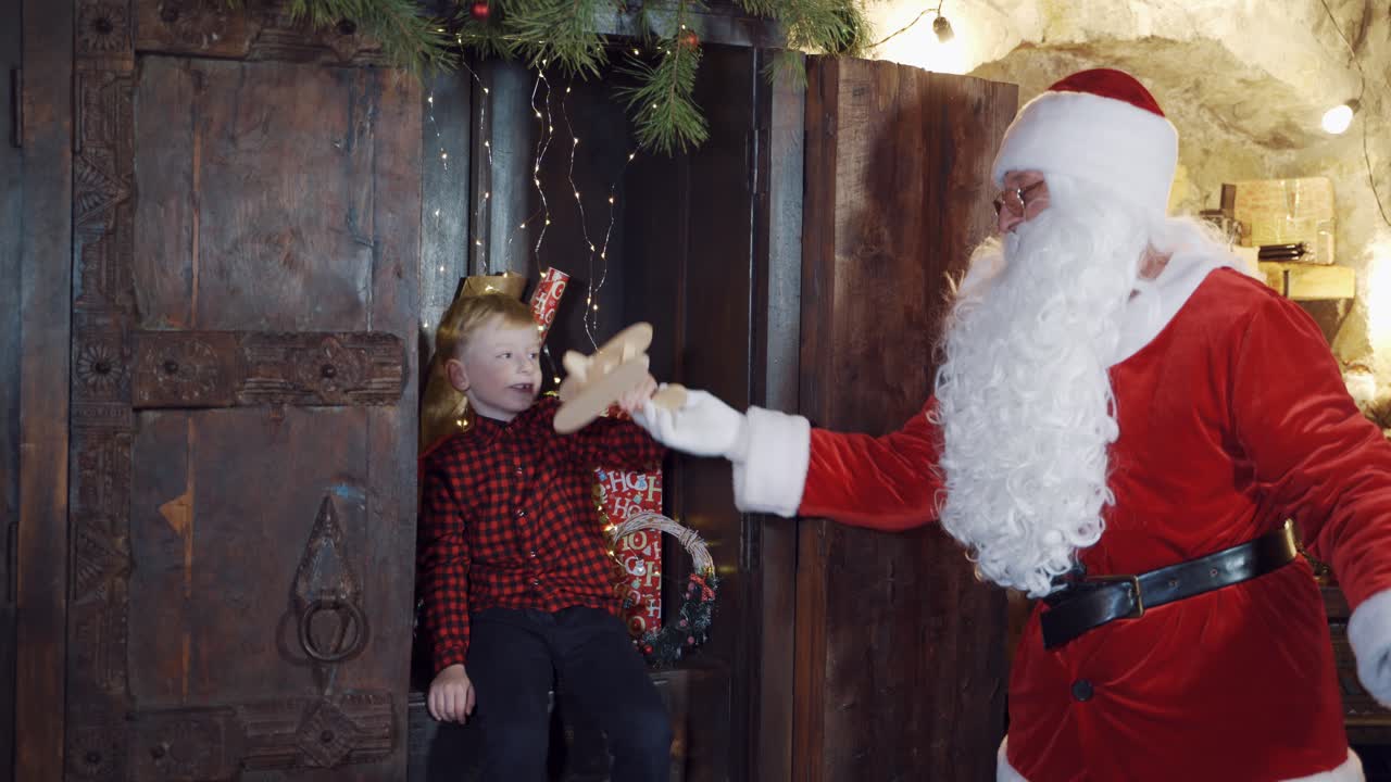 Santa gives homemade toy plane to a little boy. Christmas presents for children. Cute boy receives wooden toy from Santa inside the house.