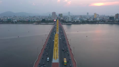 drone flying straight over dragon bridge cau rong, traffic and city skyline during sunset in danang, vietnam