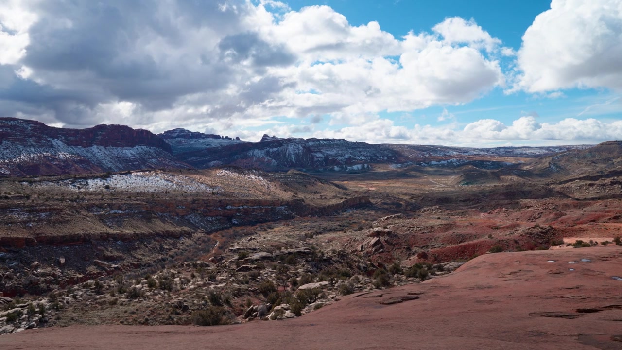 Ampia panoramica che mostra due escursionisti che scalano la montagna, rivelando poi un vasto paesaggio aperto in una giornata di sole nello Utah