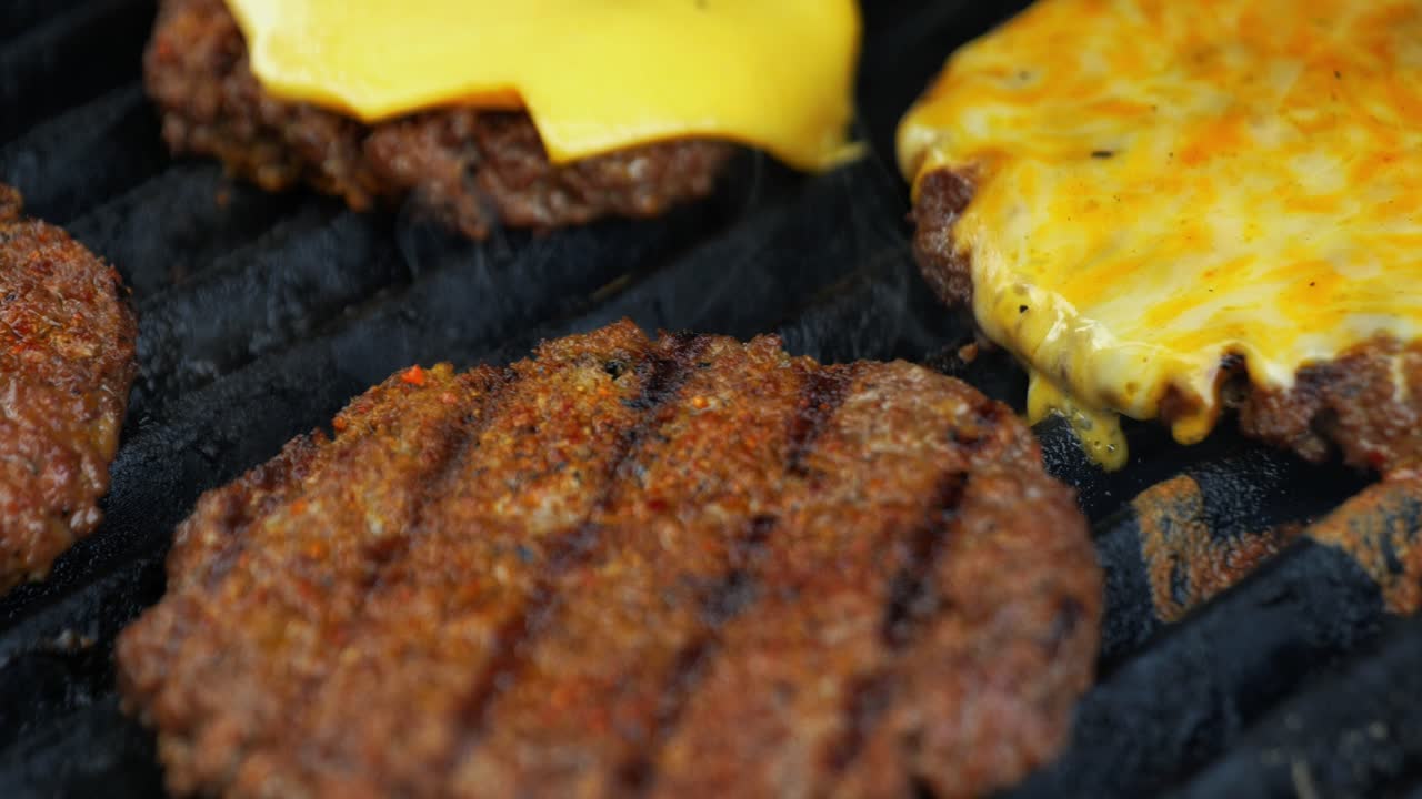 Barbecuing plant based Impossible Burger patties on electric grill close up shot panning over patty with melted cheese and smoke billowing as grill top shuts - in Cinema 4k (30fps slowed from 60fps).