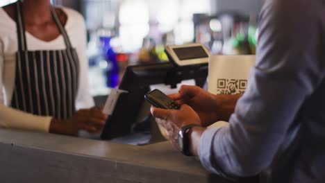 hombre de raza mixta dando a una trabajadora de café afroamericana su tarjeta de crédito para pagar