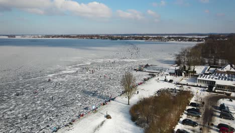 aerial flyover parking cars beside people ice skating on frozen lake in winter - netherlands,europe