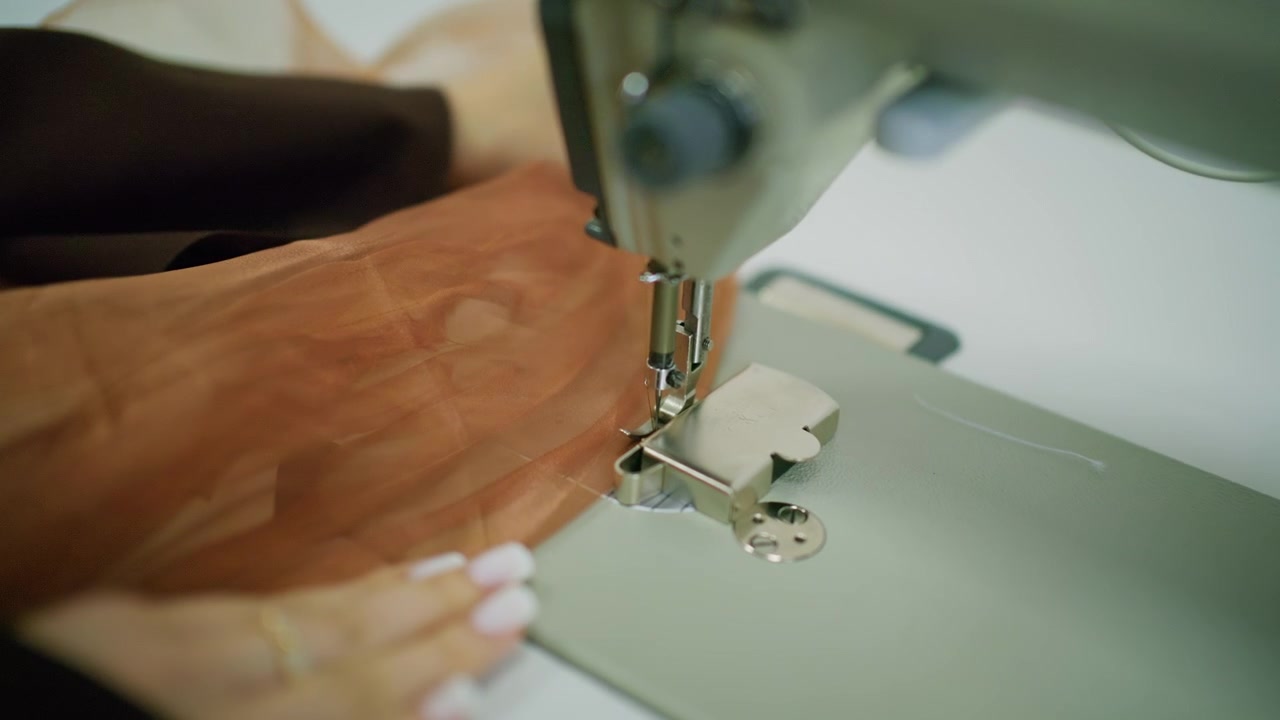 Primer plano de una persona guiando tela transparente marrón bajo la aguja de una máquina de coser industrial