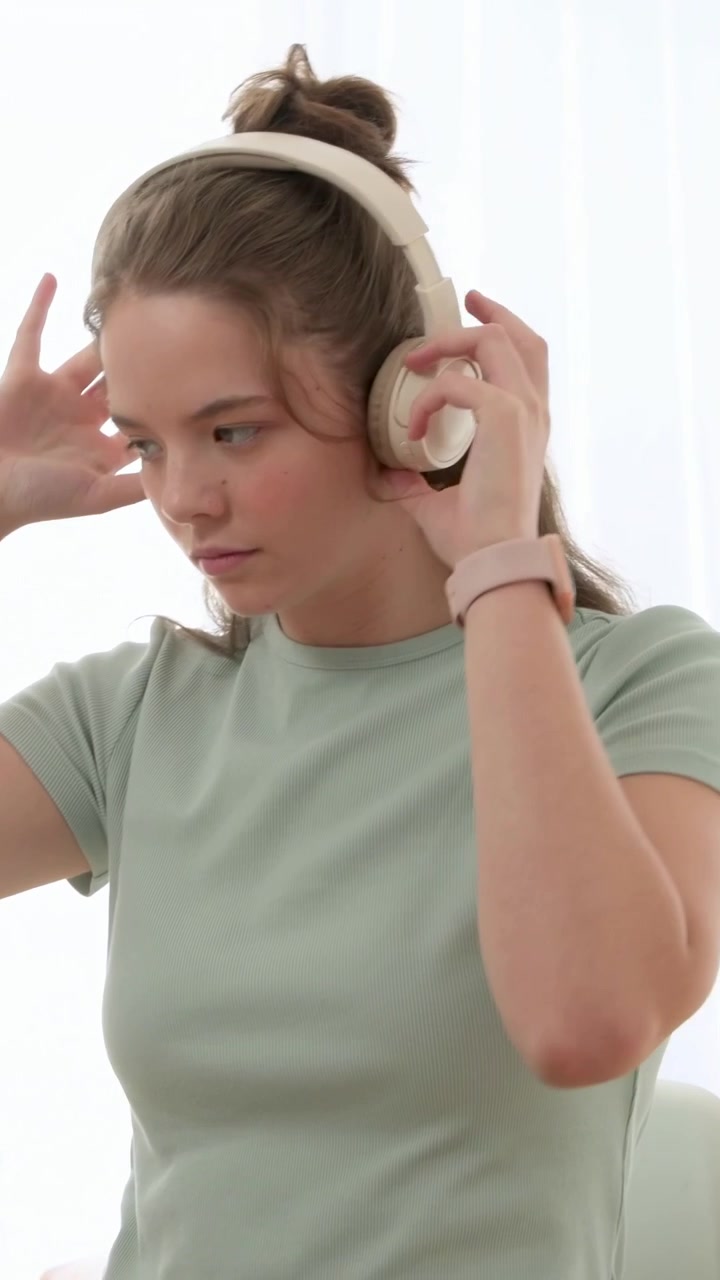 Video verticale: Una donna in maglietta color menta, tenendo una tazza beige, si toglie le cuffie al tavolo controllando gli appunti.