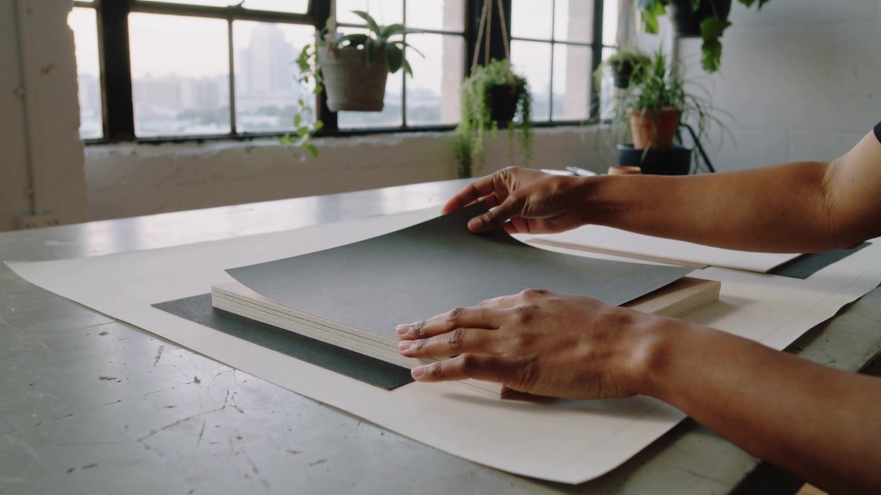 Reaching after placing pad, hands in short sleeves aligning gray sheet in studio for alignment