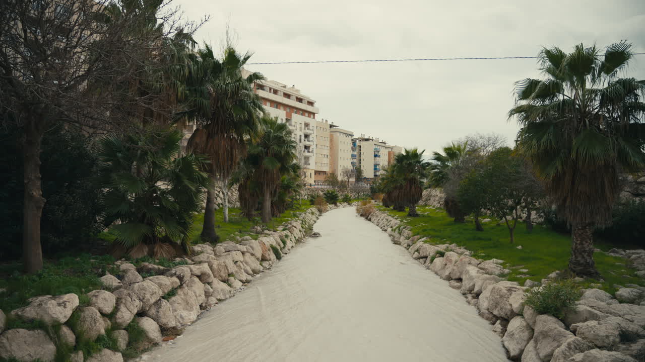 Scena urbana nuvolosa di acqua piovana torbida che scorre attraverso un canale di scolo rivestito in pietra verso il mare, evidenziando inquinamento, deflusso e cicli ambientali.