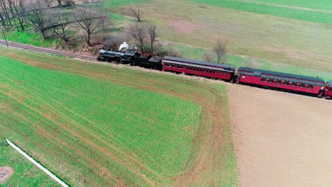 steam train puffing along amish farmland on a sunny summer day as seen by a drone