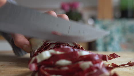 Close-up-woman's-hand-slicing-Italian-chicory-with-a-sharp-knife-on-a-wooden-board-in-her-kitchen