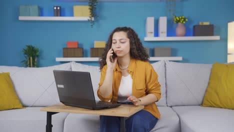 mujer joven usando una computadora portátil hablando nerviosamente por teléfono.