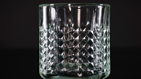 watch ice cubes fall into a textured glass against a dark backdrop, highlighting the intricate patterns.