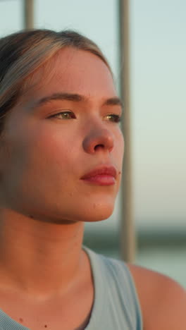 close-up of young lady with thoughtful expression as sunlight reflects off her face, sitting near iron railing during sunset, creating a moody atmosphere with blurred background