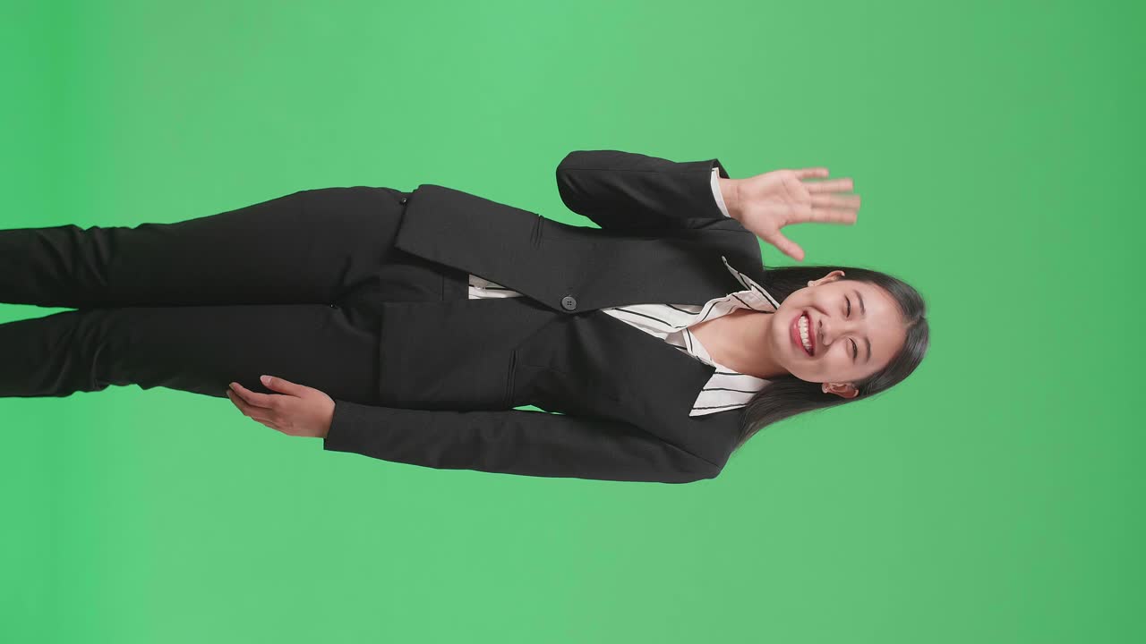 An Asian Business Woman Waving Hand And Smiling While Standing On Green Screen In The Studio