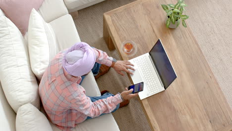 using smartphone and laptop, man working from home on couch