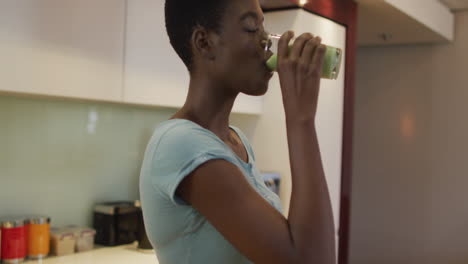 profile of smiling african american attractive woman drinking homemade smoothie in kitchen