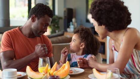 family shot with parents and daughter at home playing game at table before eating breakfast