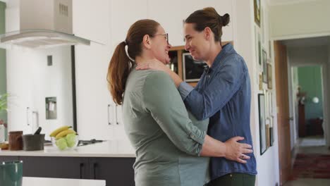 pareja de lesbianas caucásicas sonriendo y bailando en la cocina