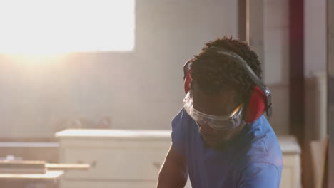 Leaning African American man cutting wood in workshop, with red earmuffs, copy space