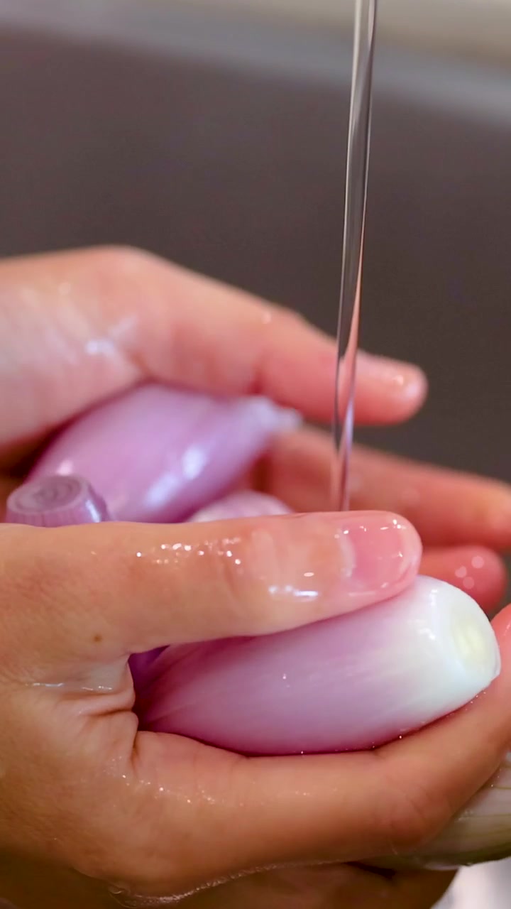 Primo piano verticale di mani che sciacquano scalogni viola sotto un getto d'acqua della cucina.