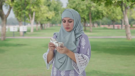 serious muslim woman counting money in park