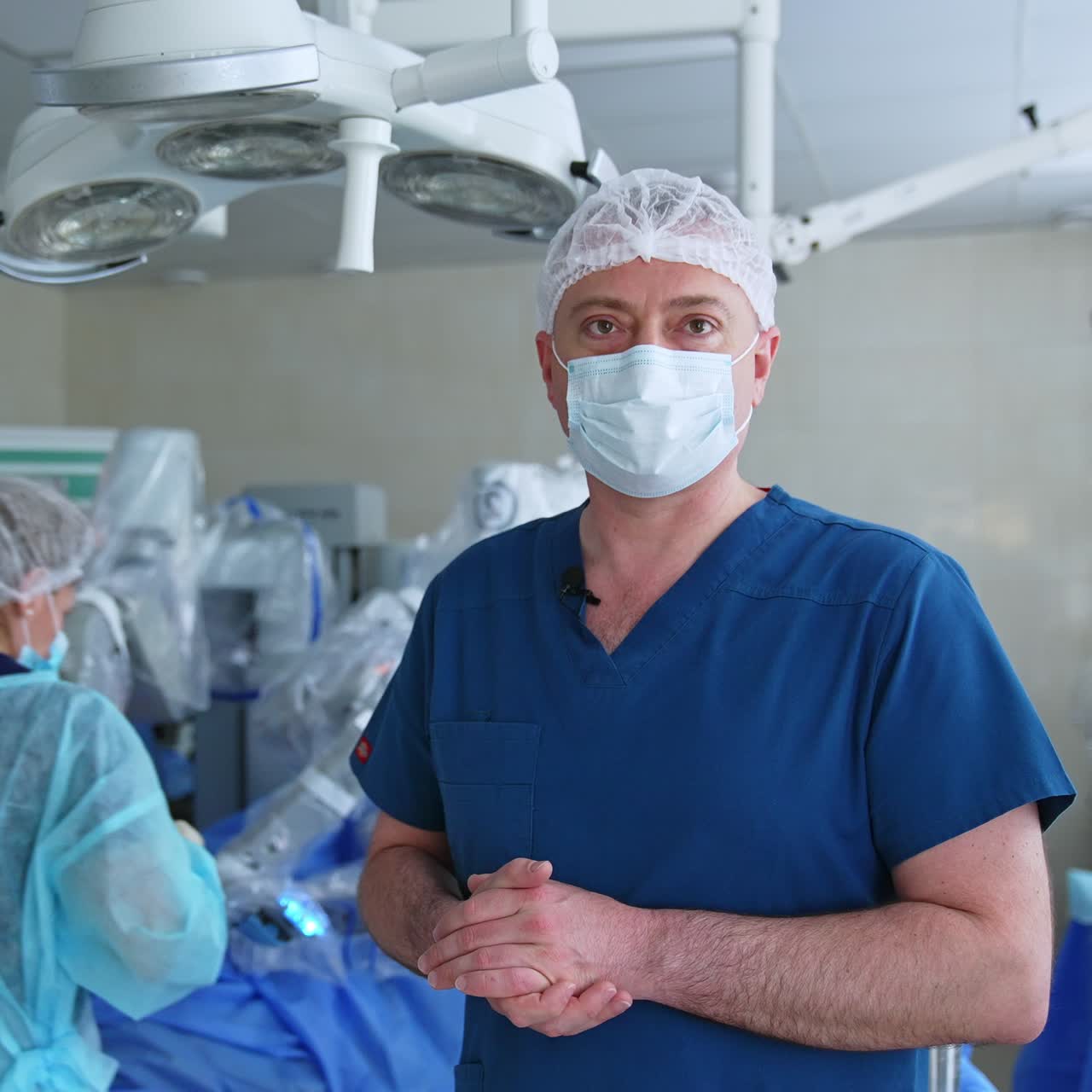 Medical team prepares Da Vinci robotic equipment for usage at the operation. Male surgeon comments the process at the foreground