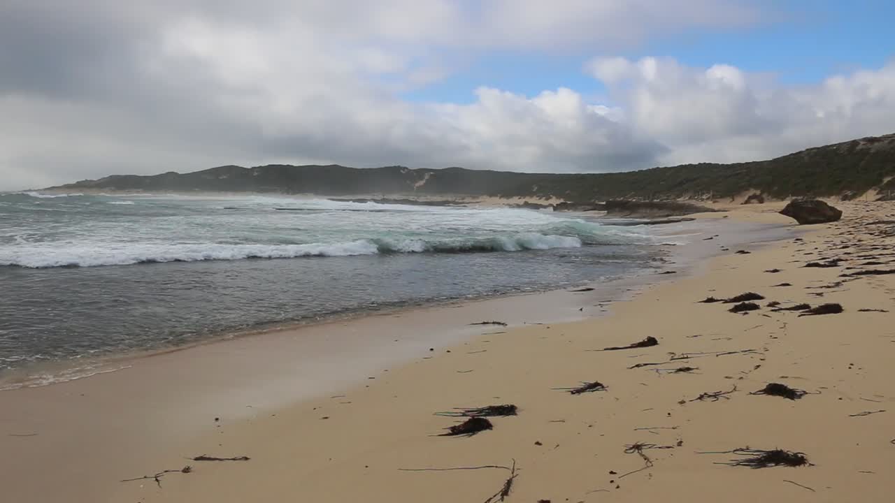 Sanfte Wellen kräuseln sich an den sandigen Ufern von Surfers Point, Margaret River, unter einem bewölkten Himmel. Dieses ruhige Weitwinkelpanorama fängt die unberührte natürliche Schönheit der australischen Küste ein.
