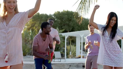 happy diverse group of friends dancing holding cocktails at beach