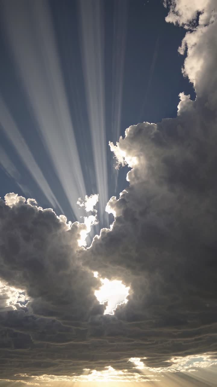 Dramatic low-angle shot of sun rays piercing through thick clouds, creating a cinematic video effect