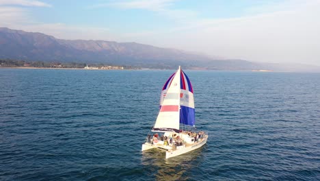 Antena-Sobre-Un-Catamarán-De-Vela-Navegando-Frente-A-La-Costa-De-Santa-Bárbara,-California