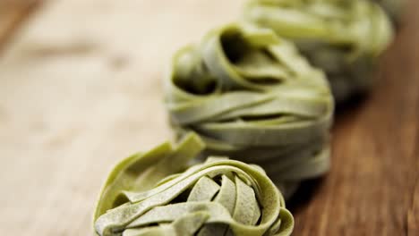 roll of green tagliatelle pasta one after another on wooden background