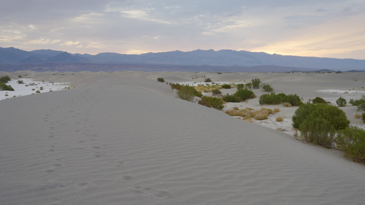 Desert Sand Dunes with Footprints and Mountains at Dusk
