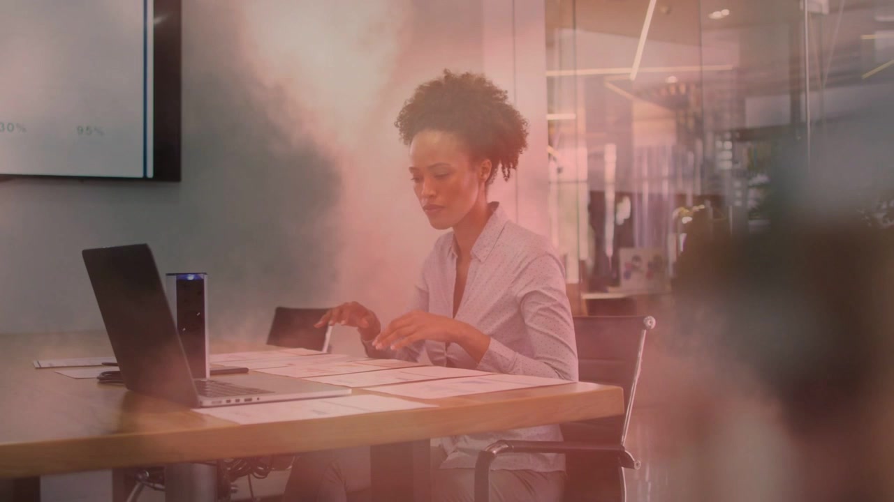 Mulher organizando papéis e digitando no laptop em uma reunião, ativando sobreposições de gráficos para um relatório de negócios.