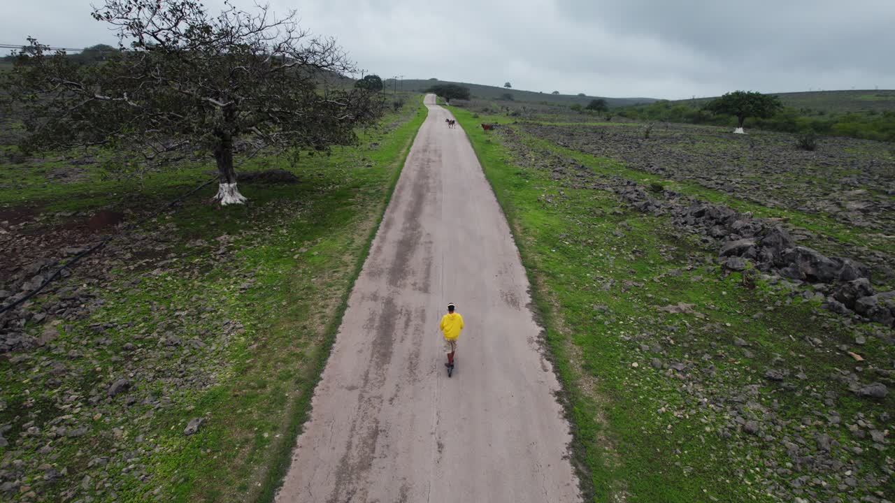 hombre montando un scooter eléctrico en la naturaleza en un clip de drone de carretera