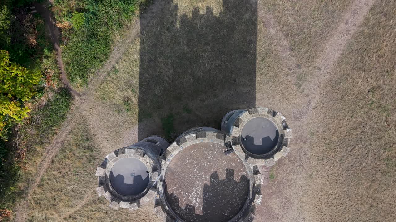 Aerial top-down drone shot above grass, showing shadows of Blaise Castle’s turrets. As the drone pulls back, the historic castle emerges from the shadow