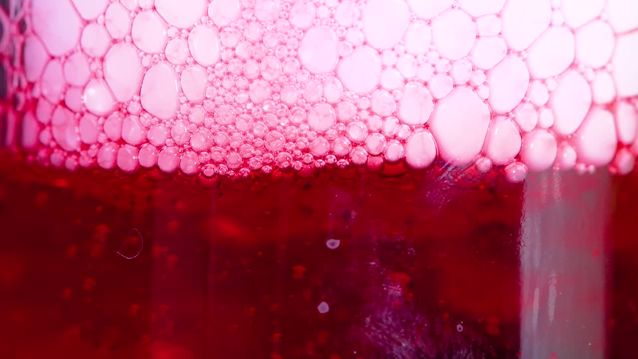 un líquido rojo vibrante con burbujas se forma a medida que el hielo seco reacciona, creando un efecto visual dinámico en un recipiente de vidrio