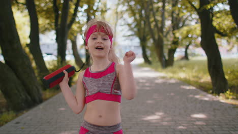 Sport-runner-jogger-child-girl-listen-bluetooth-music-speaker-dancing-to-camera-having-fun-in-park