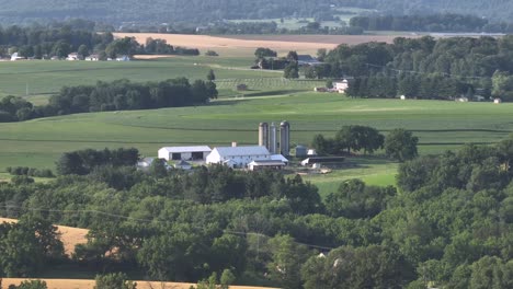 aerial view of picturesque american farm with lush green fields and charming farm buildings. rolling hills stretch into the distance under bright foggy sky. peaceful rural farmstead in usa
