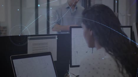 Animation-of-glowing-network-over-smiling-businesswoman-using-computers-in-office