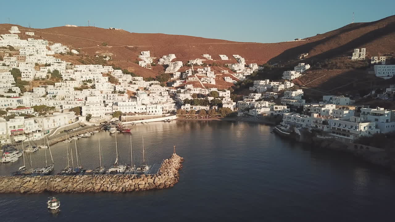 Greece, Astypalea Harbor and the town view early in the morning, a vessel is landing slowly to the dock behind the harbor on a sunny day.