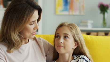 Close-Up-Of-The-Smiled-Pretty-Mother-And-Daughter-Sitting-On-The-Yellow-Couch-And-Talking-In-The-Living-Room