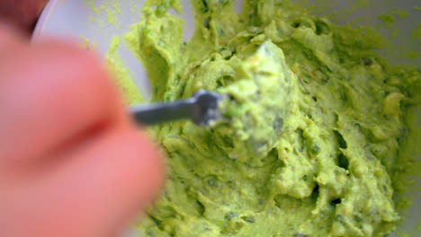 stirring mashed avocado using spoon in a bowl