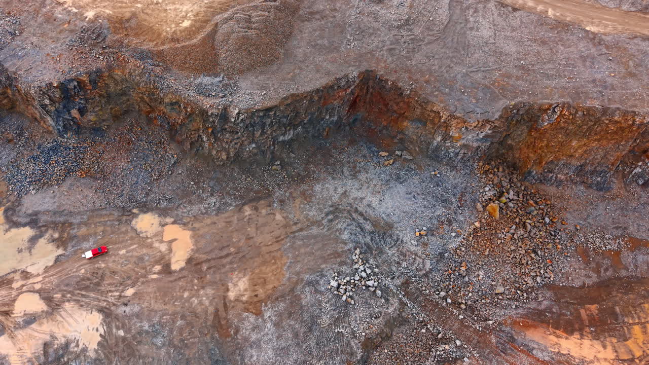 Aerial top view of stone quarry wall and red vehicle. High angle shot of rocky cliff texture with red truck on ground level in an open pit mine