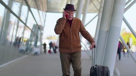 senior tourist grandfather man walking on international airport hall using mobile phone conversation