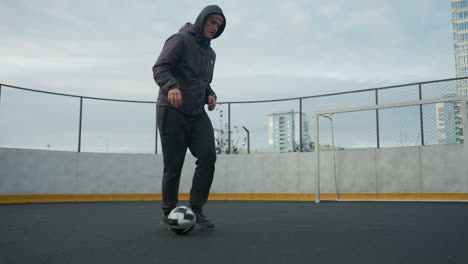 young man skillfully controlling soccer ball with precise footwork on sport arena, showcasing balance, agility, and athleticism, background includes urban architecture and blurred goal