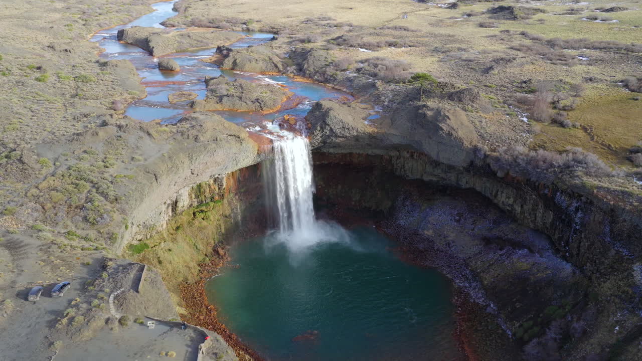 Agrio Waterfall near Caviahue, Neuquén Province, Argentina, showing the Agrio River cascading over basalt cliffs into a turquoise volcanic pool surrounded by rugged steppe, drone orbit