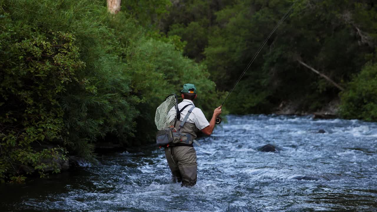 Fly fisherman wades upstream through a fast mountain river