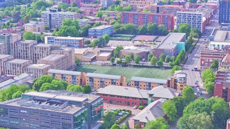 aerial of manchester, united kingdom, capturing a synthetic turf football field surrounded by student housing, academic buildings, and dense city blocks in the university area near dilworth street