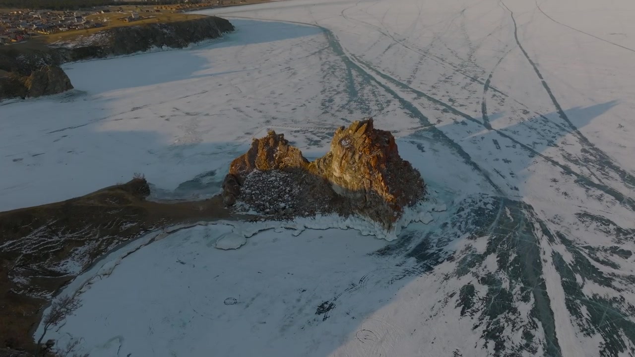 Dronekuvaa Šamanka-kalliosta Olkhon-saarella, jäätyneen Baikaljärven ympäröimänä jäänhalkeamien ja jälkien kera, talvimaisema lähellä Khuzhiria, Irkutskin alueella, Venäjällä.